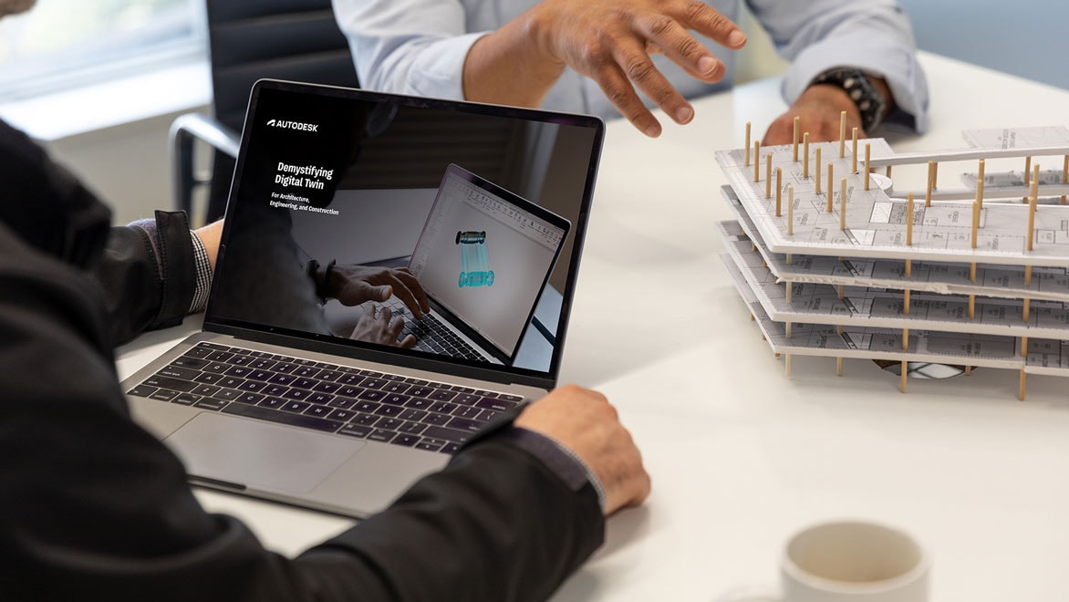  A laptop on a conference table next to a building model displays the Demystifying Digital Twin e-book